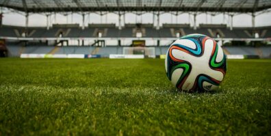 Close-up of a soccer ball on a lush grass field with an empty stadium in the background.